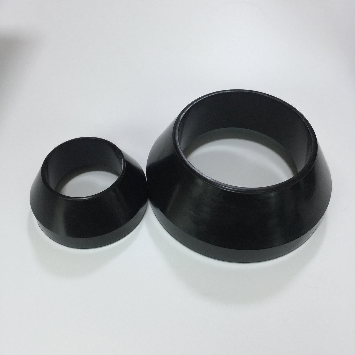 Two black molded conical rubber packer elements in different sizes
