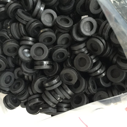Black molded rubber grommets in a production batch with center openings and grooved outer walls